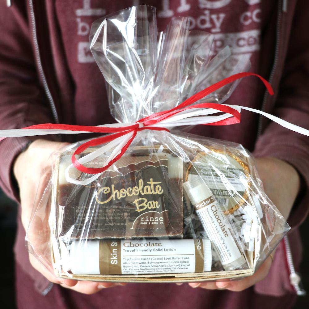 Hands holding a cellophane-wrapped chocolate gift basket against a maroon hoodie — red-and-white bows catching studio light