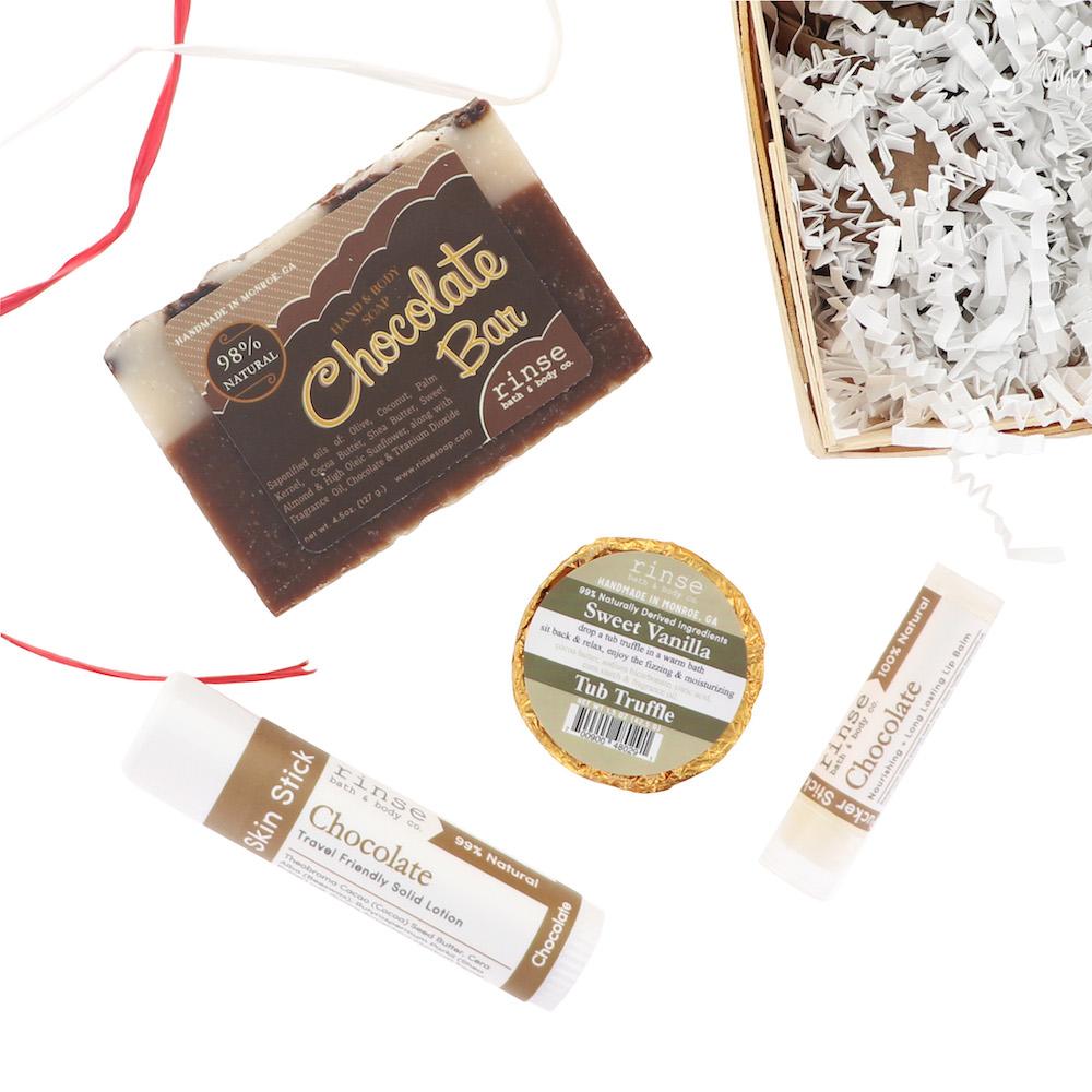 Chocolate Bar Soap Skin Stick Pucker Stick and Sweet Vanilla Tub Truffle scattered with red ribbons — flat lay on bright white