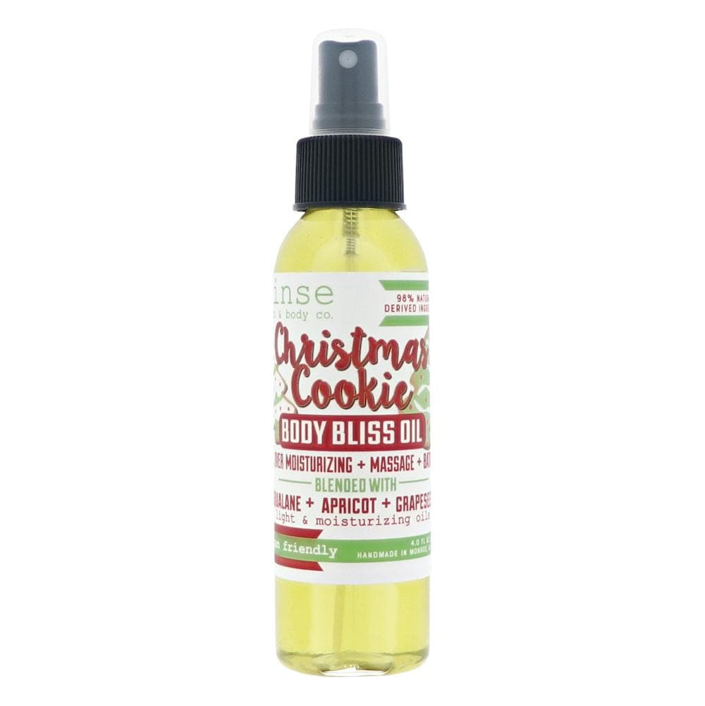Christmas Cookie Body Bliss Oil standing on bright white — festive red-green label and golden oil in studio light