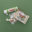 The Christmas Cookie gift set on sage paper scattered with snow and red-and-white sprinkles — bar soap, solid lotion skin stick and lip balm. Rinse Bath & Body Co.
