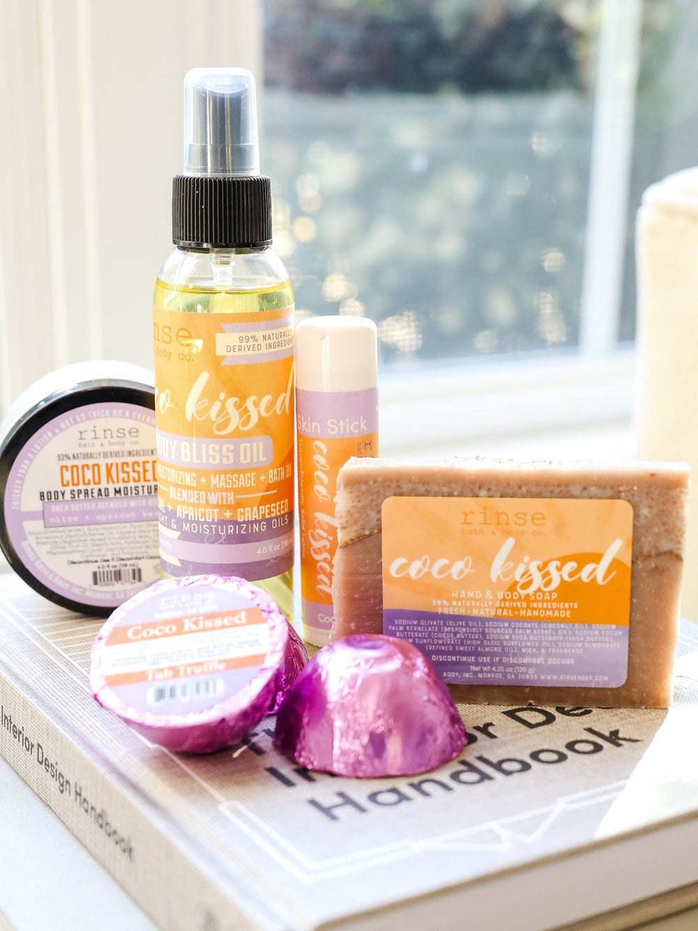 Coco Kissed lineup rests on The Interior Design Handbook — purple foil catching bright window light