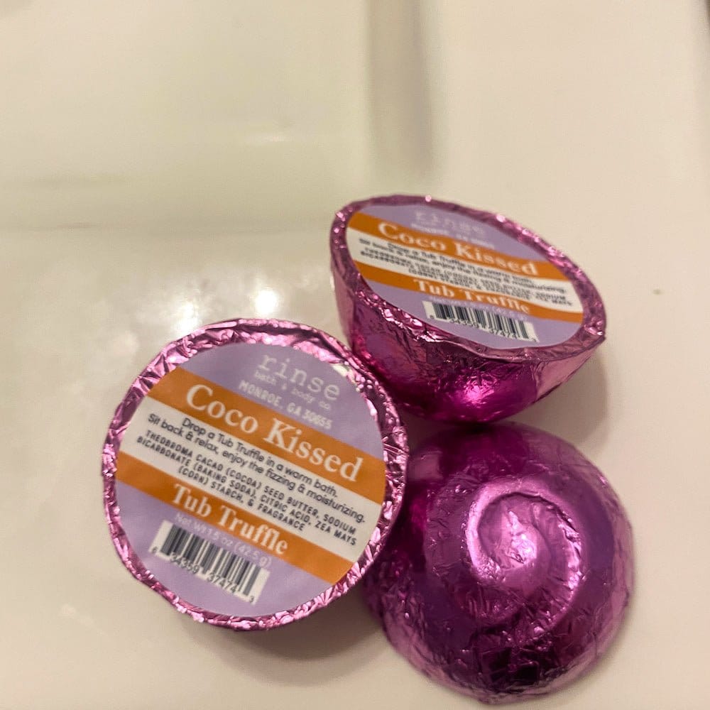 Three pink-foil Coco Kissed Tub Truffles rest on white porcelain — metallic wrap catching studio light