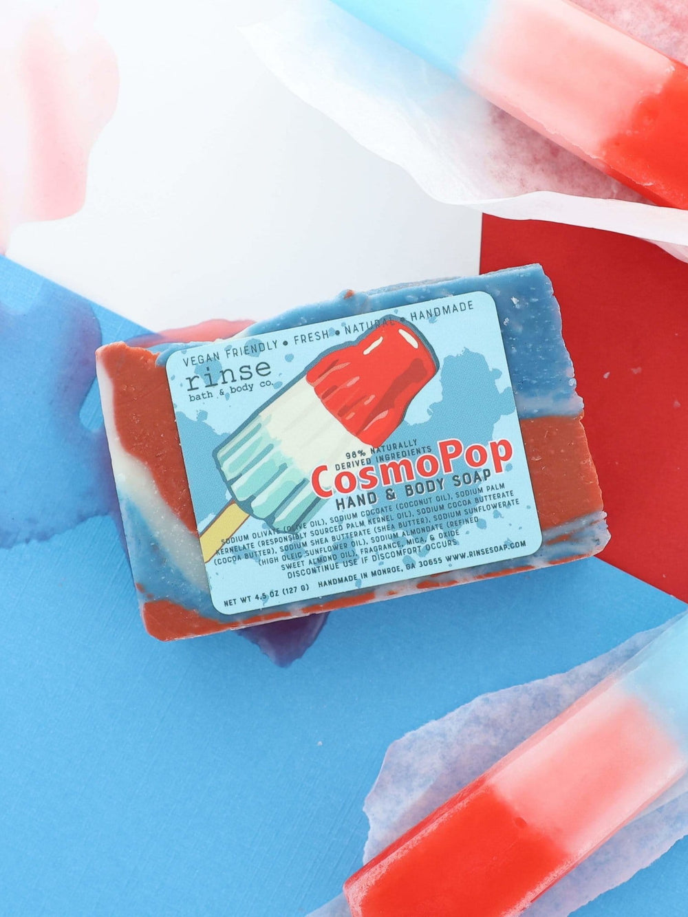 Labeled CosmoPop bar centered on red-blue split — popsicle tips and blue splash in bright flat light