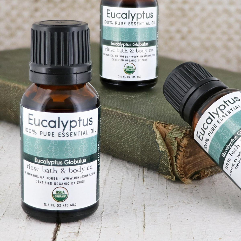 Three Eucalyptus essential oil bottles with a vintage green book on weathered white wood — amber glass and leaf-banded labels in soft light
