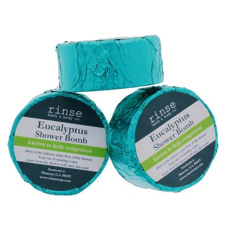 Three Eucalyptus Shower Bombs stacked in crinkled teal foil — steam-ready pucks on clean white studio light