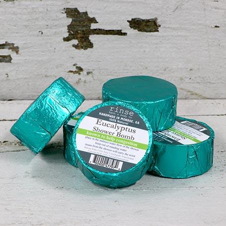 Five teal-foil Eucalyptus Shower Bombs rest on peeling white wood — rustic cracks under bright flat light
