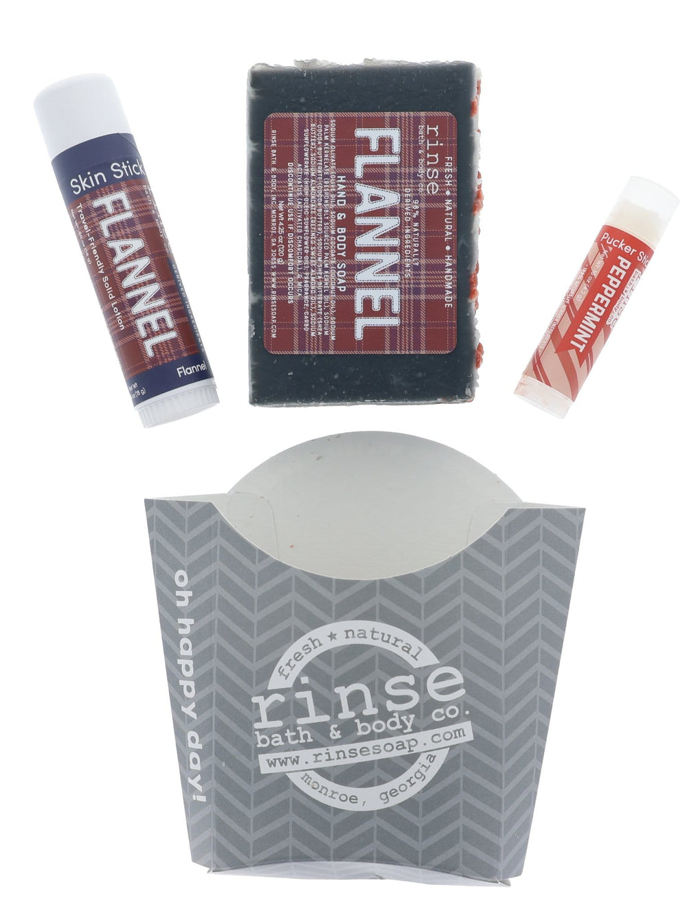 The Flannel fry-box set laid out flat — bar soap, solid lotion stick, lip balm and the printed kraft carton they arrive in. Rinse Bath & Body Co.