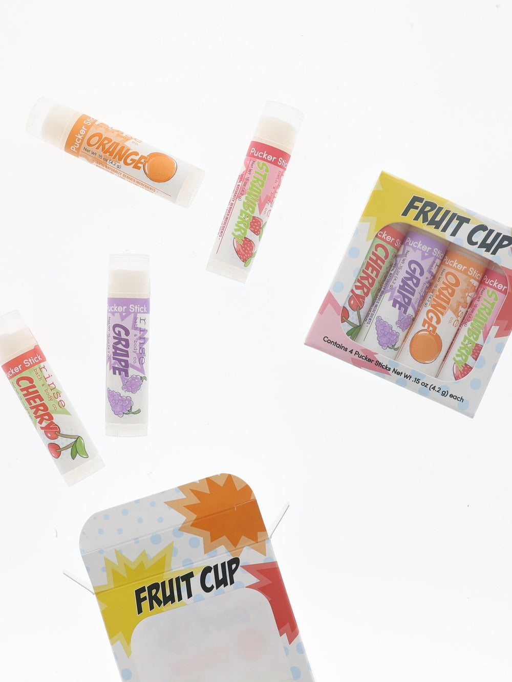 Fruit Cup set and loose Pucker Sticks floating on bright white — comic-pack carton and fruit tubes scattered in high-key light