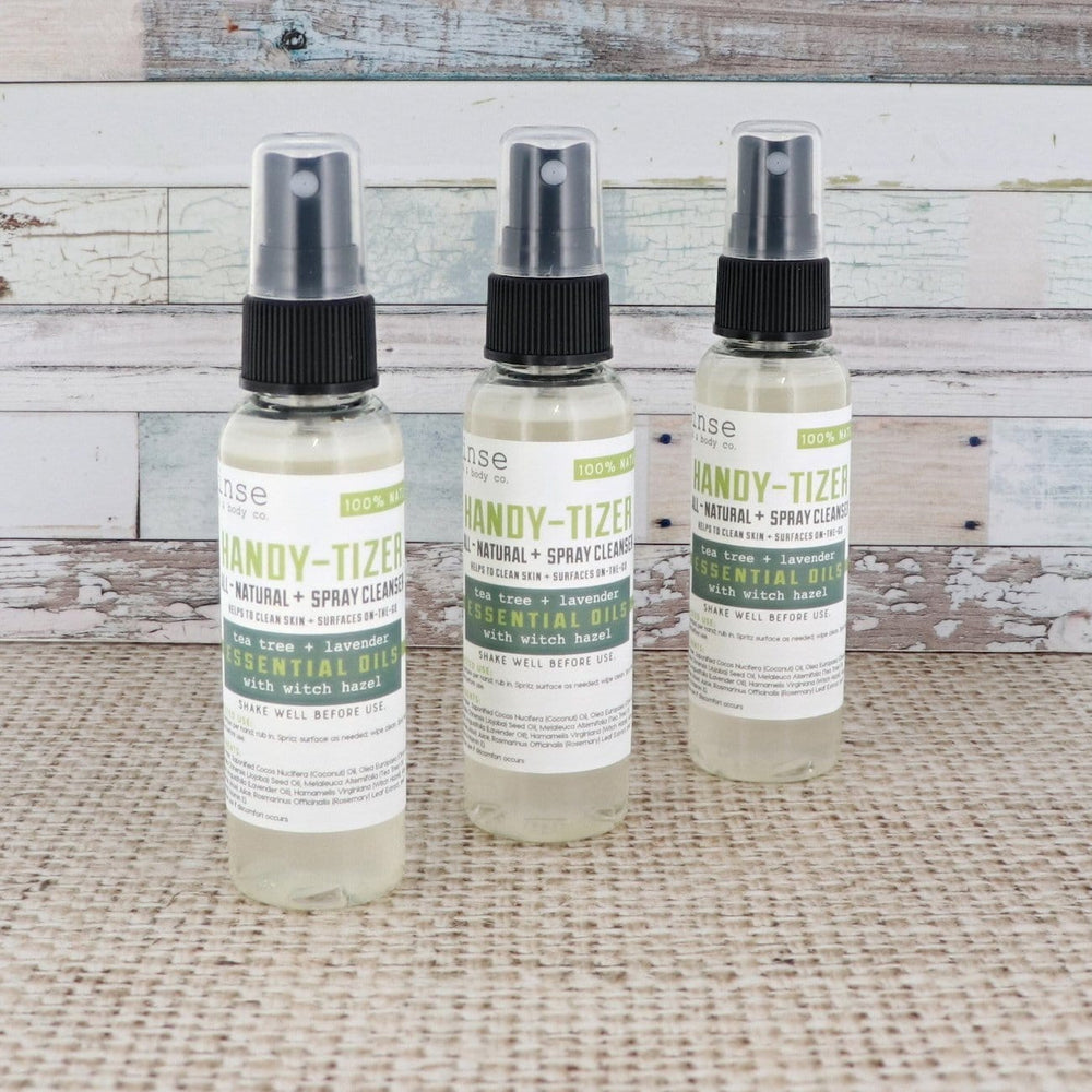 Three Tea Tree + Lavender Handy-Tizer bottles stagger on tan burlap — weathered white and blue wood behind