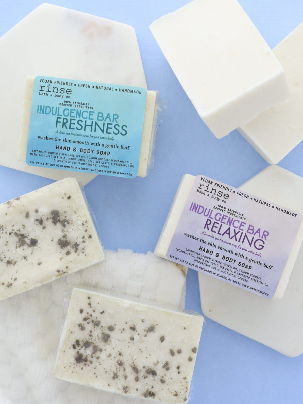 Indulgence Bars arranged on marble tiles and waffle cloth — labeled wraps beside salt-chunk undersides in spa blue light