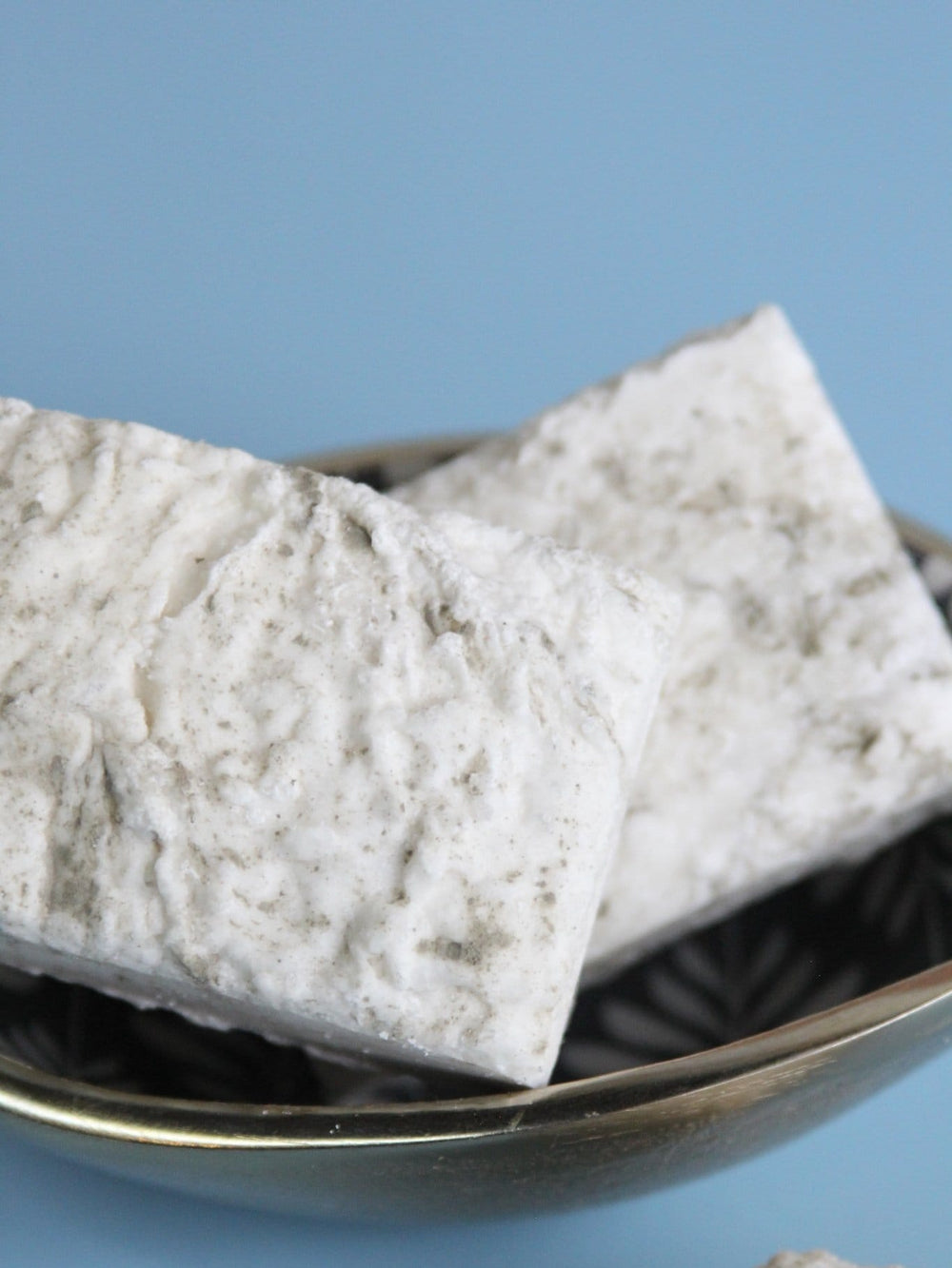 Close-up of textured Indulgence bars in a patterned bowl — porous white salt surface catching cool daylight