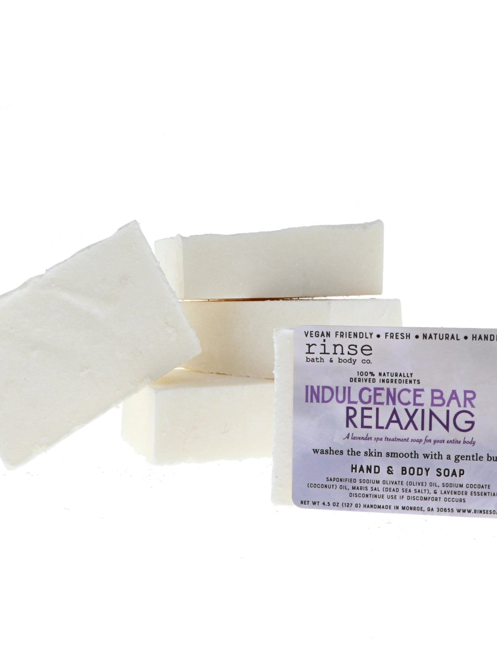 Stack of creamy Indulgence Bar Relaxing soaps with one leaning — purple label on stark white