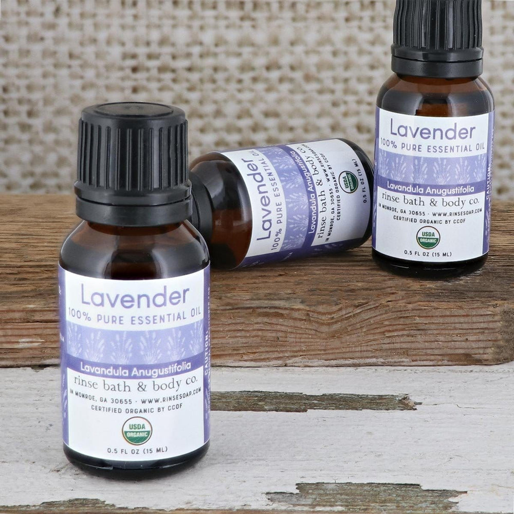 Three Lavender essential oil bottles resting on weathered wood — amber glass against soft linen light