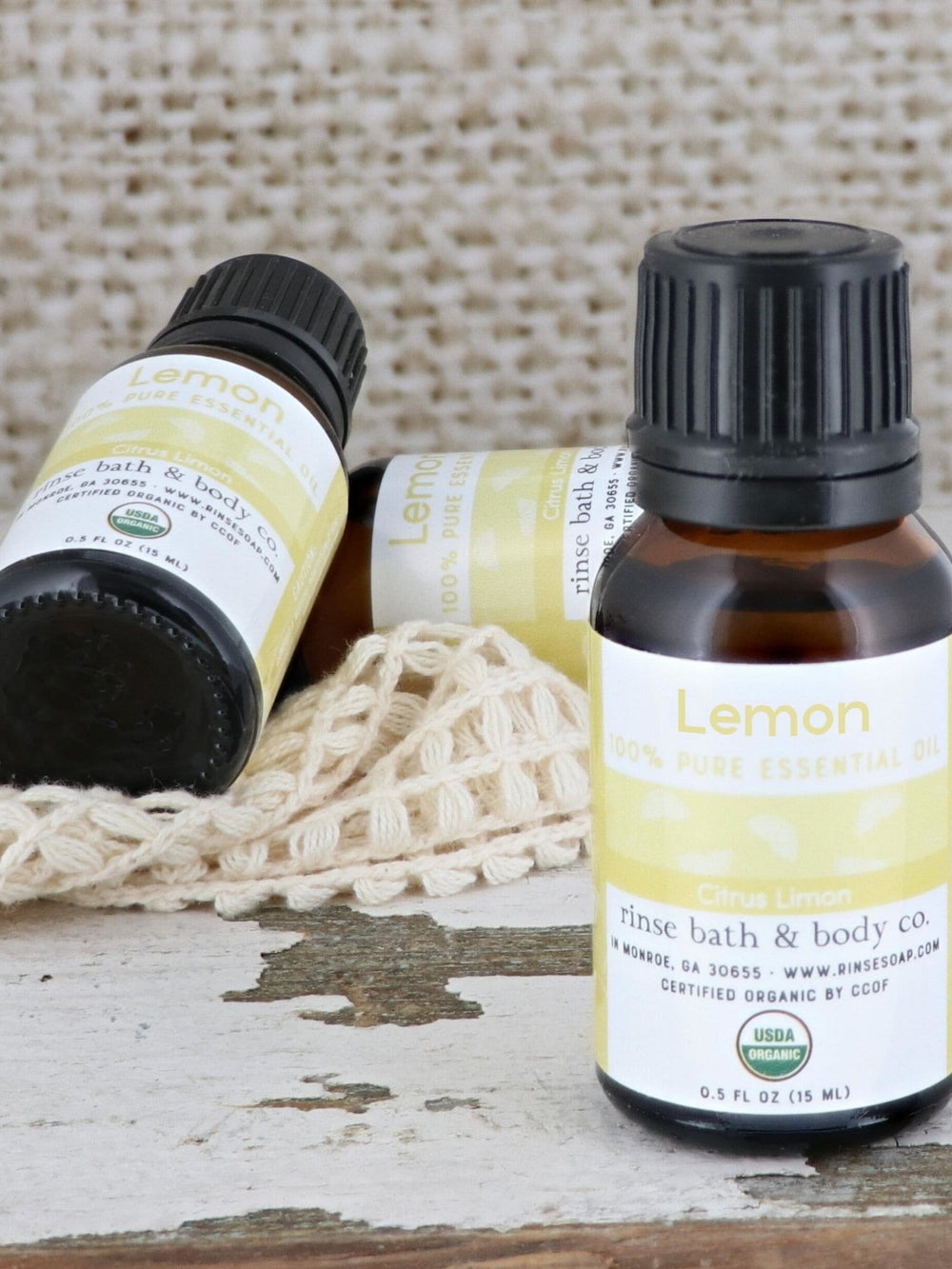 Lemon oil upright and lying on cream mesh over weathered white wood — rustic bright daylight