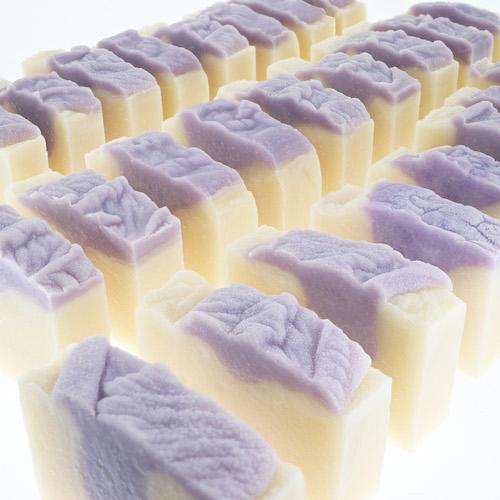 Rows of Lilac soap recede showing wavy purple tops — creamy bases in soft bright studio light