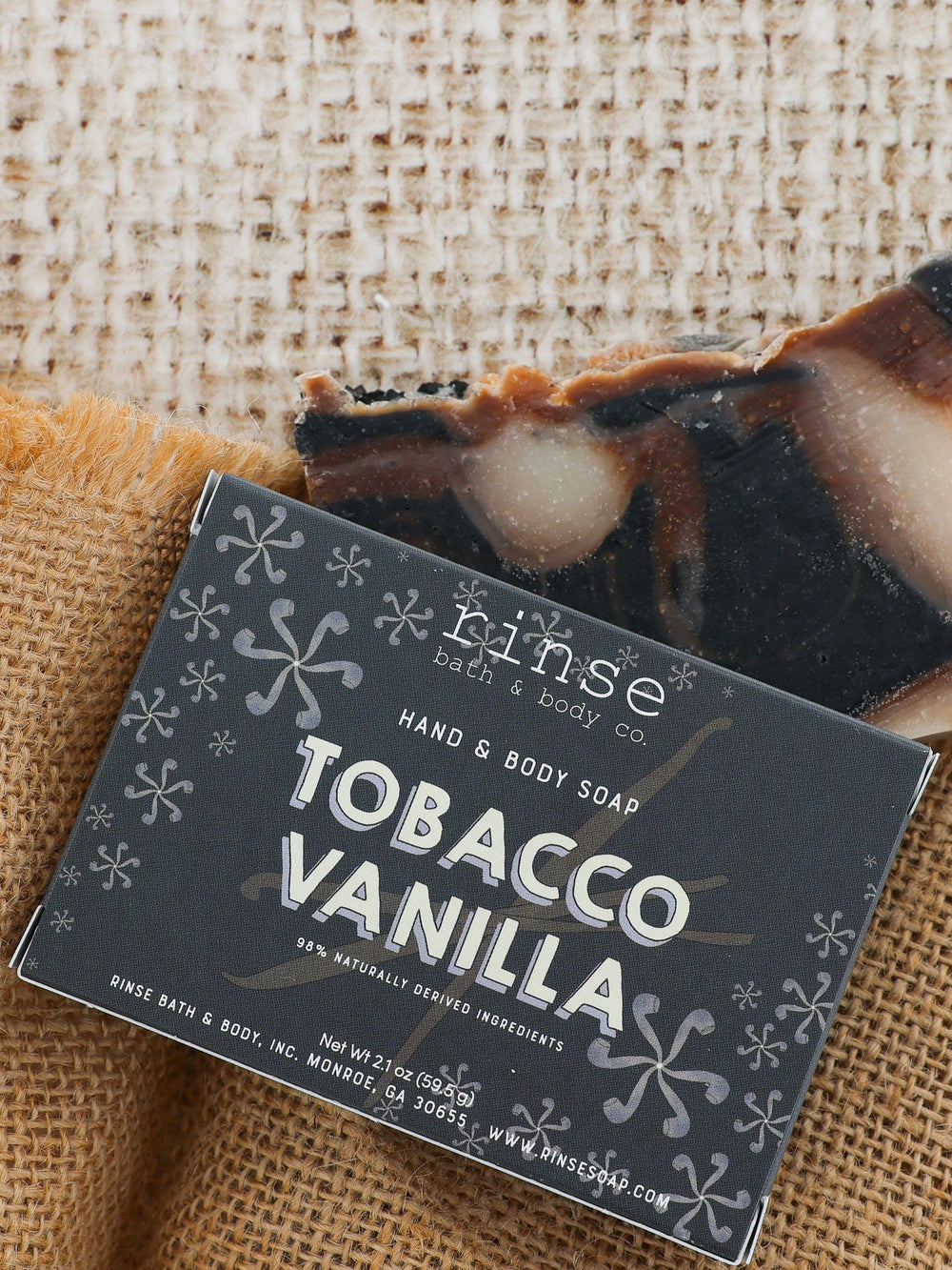 Tobacco Vanilla bar peeking behind charcoal box on golden burlap — earthy tobacco and soft vanilla