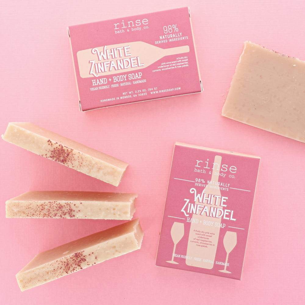 Speckled pink soap bars and boxes scatter on solid pink — White Zinfandel sleeves in a flat lay