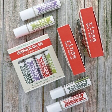 Two roll-on gift boxes and four scent bottles scattered on weathered gray wood — rustic tabletop in natural light