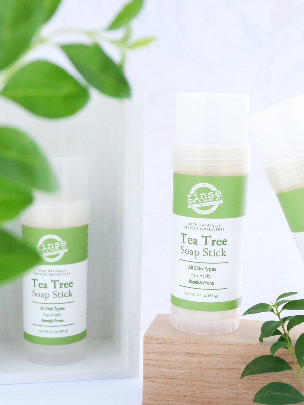 Three Tea Tree Soap Sticks arranged on light wood with soft green leaves — bright airy setting for twist-up cleansing sticks