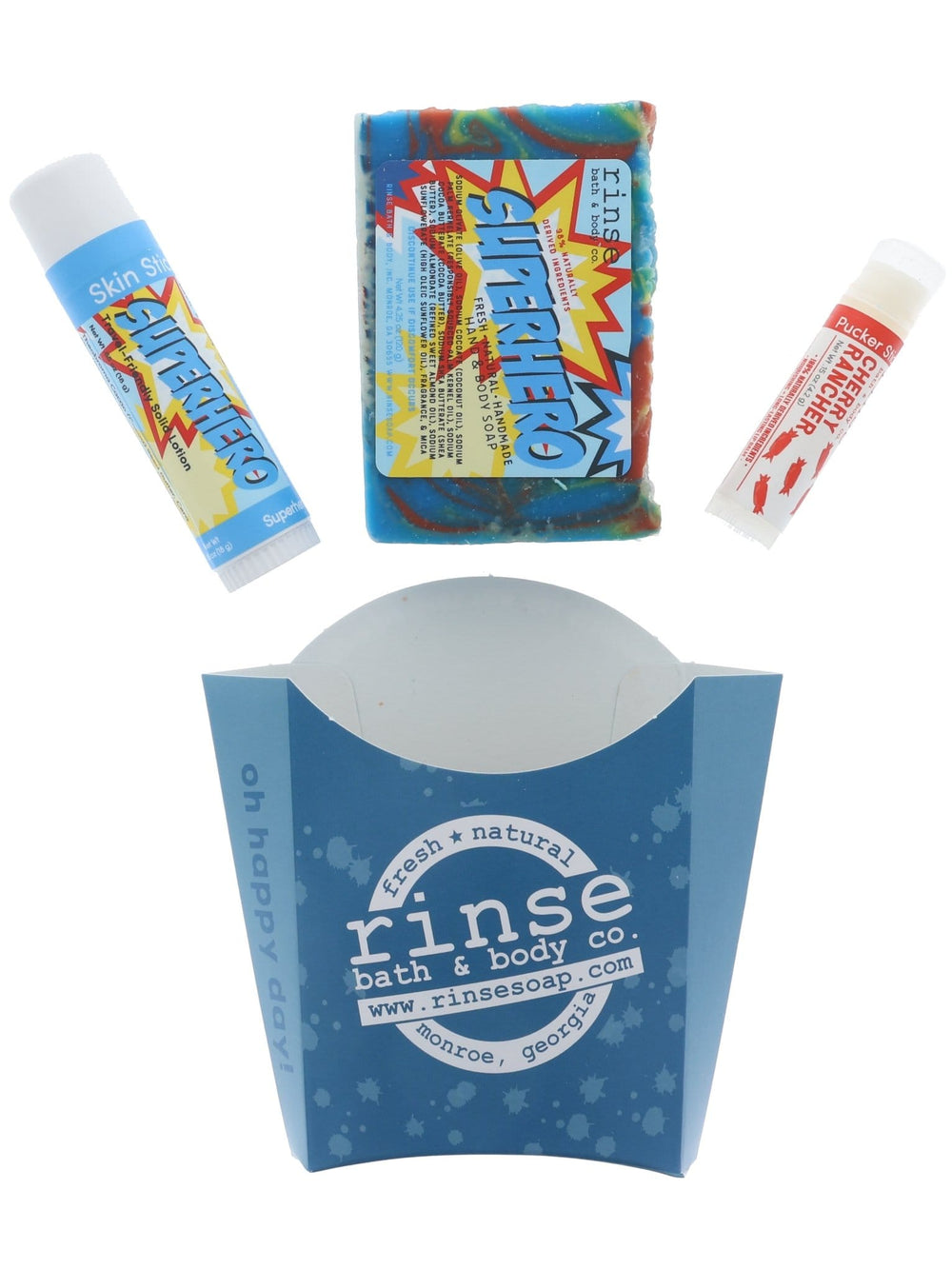 The Superhero set laid out flat — rainbow-swirl bar soap, Superhero solid lotion skin stick and Cherry Rancher lip balm above the blue carton. Rinse Bath & Body Co.