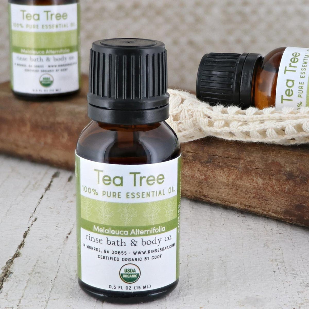 Tea Tree essential oil resting against weathered wood with a knit cloth nearby — amber glass and sage label in soft natural light