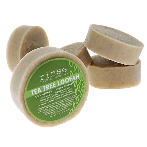 Round Tea Tree Loofah soap leans against a stack of tan disks on clean white studio.