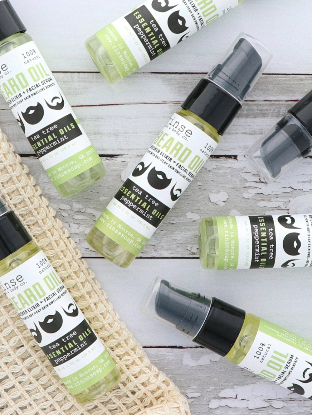 Tea Tree Mint Beard Oil bottles overlapping on distressed gray wood — green-tinted oil by a natural fiber bag