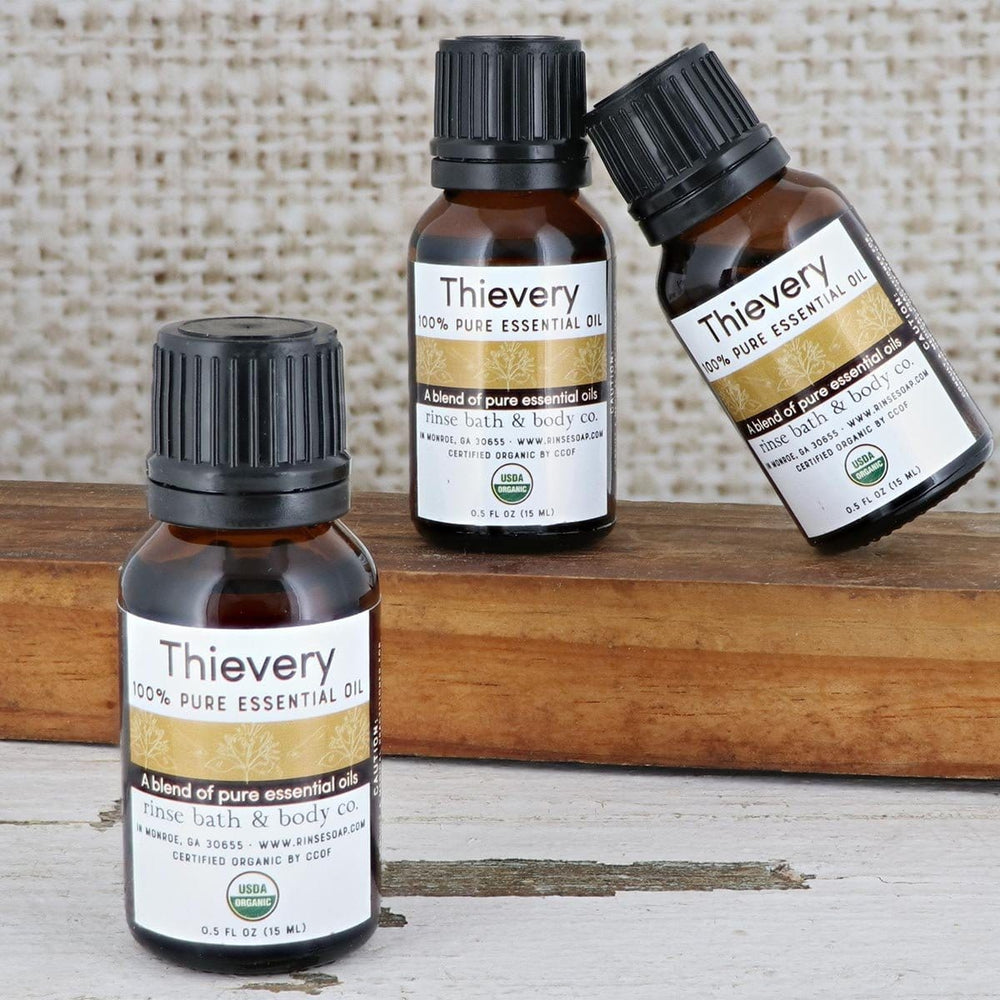 Three amber Thievery oil bottles on distressed white wood and a natural block — woven fabric soft behind
