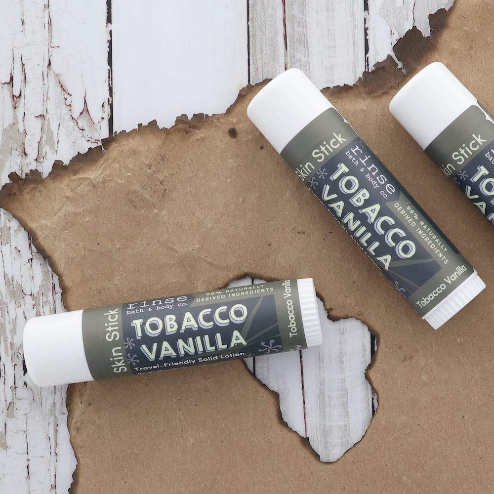 Three Tobacco Vanilla Skin Sticks on charred-edge brown paper — weathered white wood grain underneath