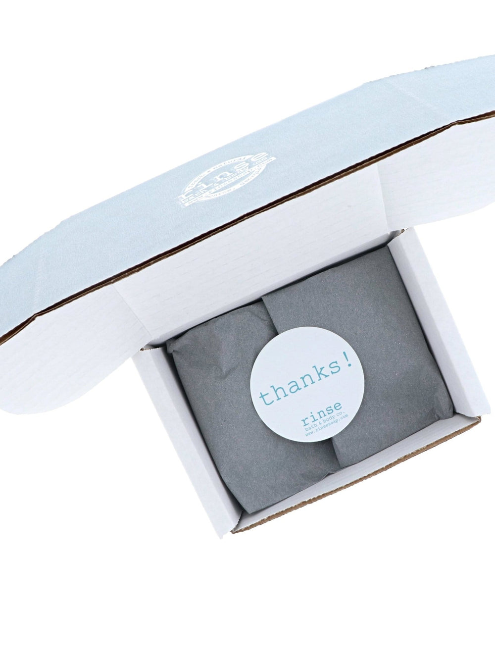 Open discovery box folds dark grey tissue under a white thanks! seal on a stark white backdrop.