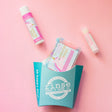 The Unicorn Magic kids gift set on pink linen — swirled unicorn bar soap, Unicorn Magic solid lotion stick and a Cotton Candy lip balm beside the aqua carton. Rinse Bath & Body Co.