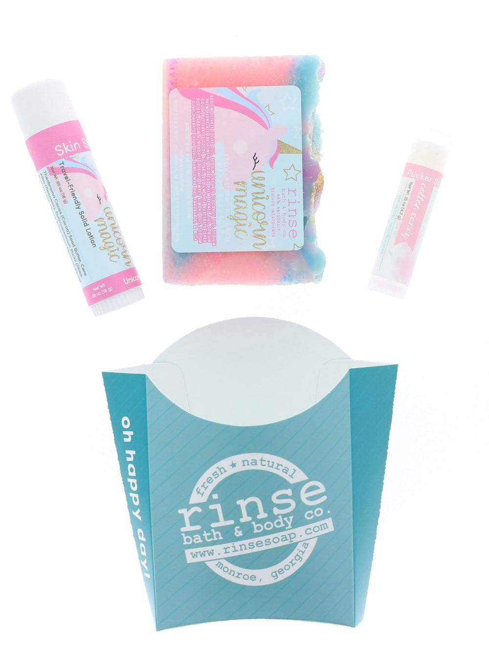 The Unicorn Magic set laid out flat — swirled bar soap, Unicorn Magic skin stick and Cotton Candy lip balm above the aqua printed carton. Rinse Bath & Body Co.