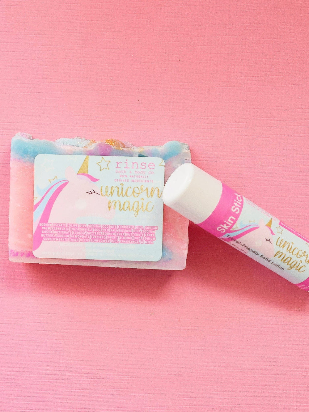 Unicorn Magic Skin Stick uncapped against swirled soap on hot pink — creamy balm tip in studio light