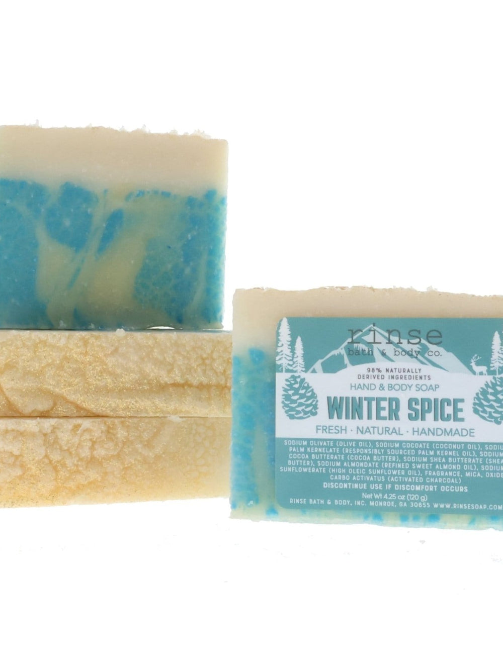 Winter Spice soap bars rest on white — cream tops over icy blue marble, teal mountain-scene labels.